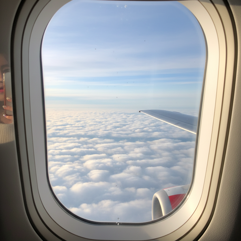 비행기 창문 너머로 보이는 푸른 하늘과 구름, 날개 끝이 살짝 보이는 감성적인 구도